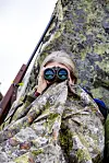 Kvinne i Jervenduk, kamuflasjeduk med kikkert og rifle på villreinjakt, reinsjakt i høyfjellet, på Reinsjøfjell.