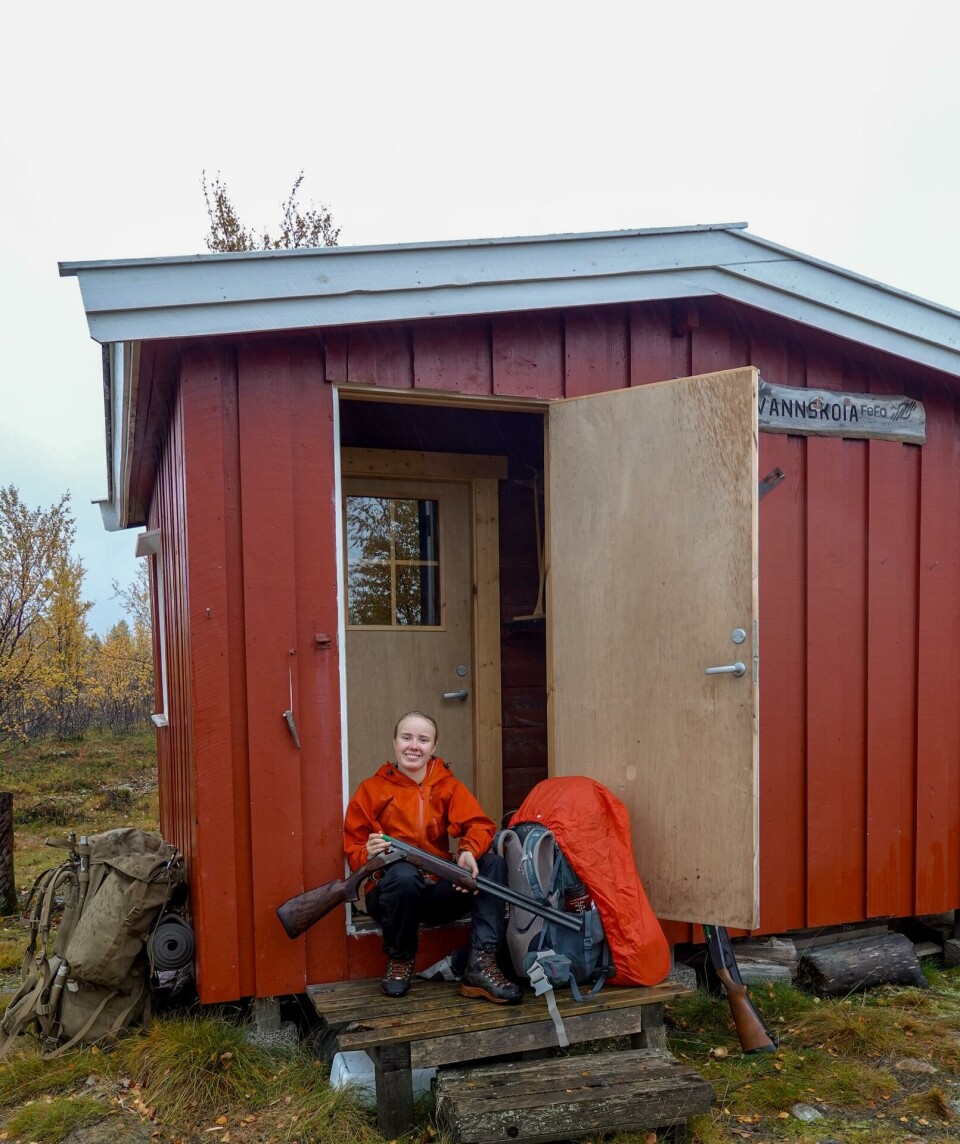 Jakttur i Pasvik høsten 2023. Karen på jakttur i Pasvik høsten 2023. Her sitter hun ved en rød hytte med hagla i hånda.