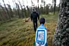 Hånd som holder lydmåler med skjerm synlig i en skog, uskarp person i bakgrunnen.