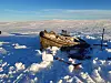 En gammel båt ligger delvis begravd i snø på et fjellplatå med blå himmel.